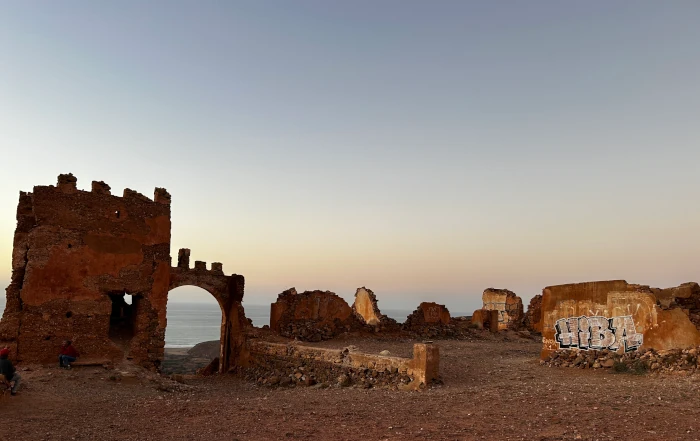 Historische Überreste einer Festung in Mirleft bei Sonnenuntergang, mit marokkanischer Küstenlandschaft im Hintergrund.